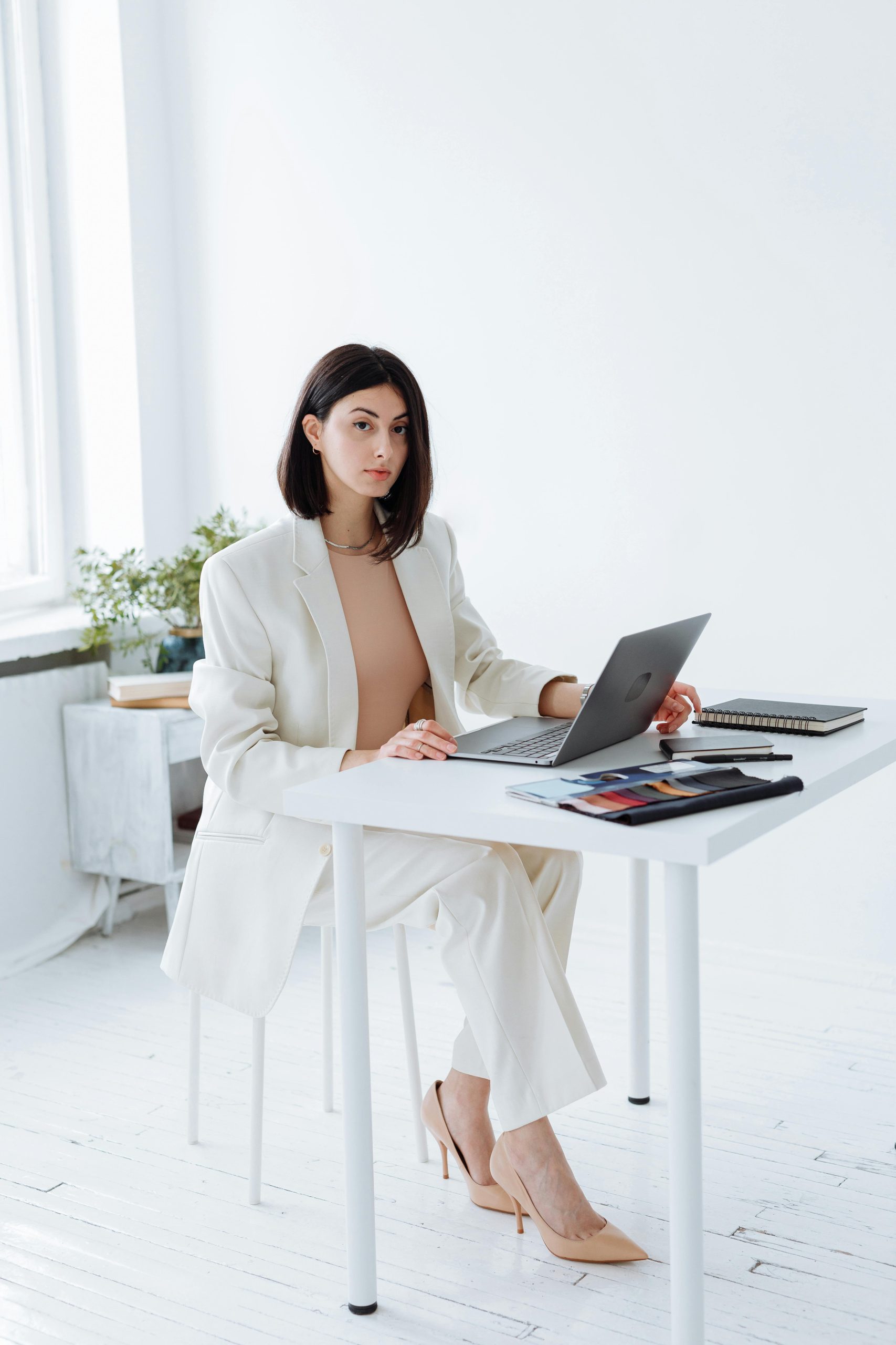 Elegant businesswoman in a white blazer working on a laptop in a bright, modern office.